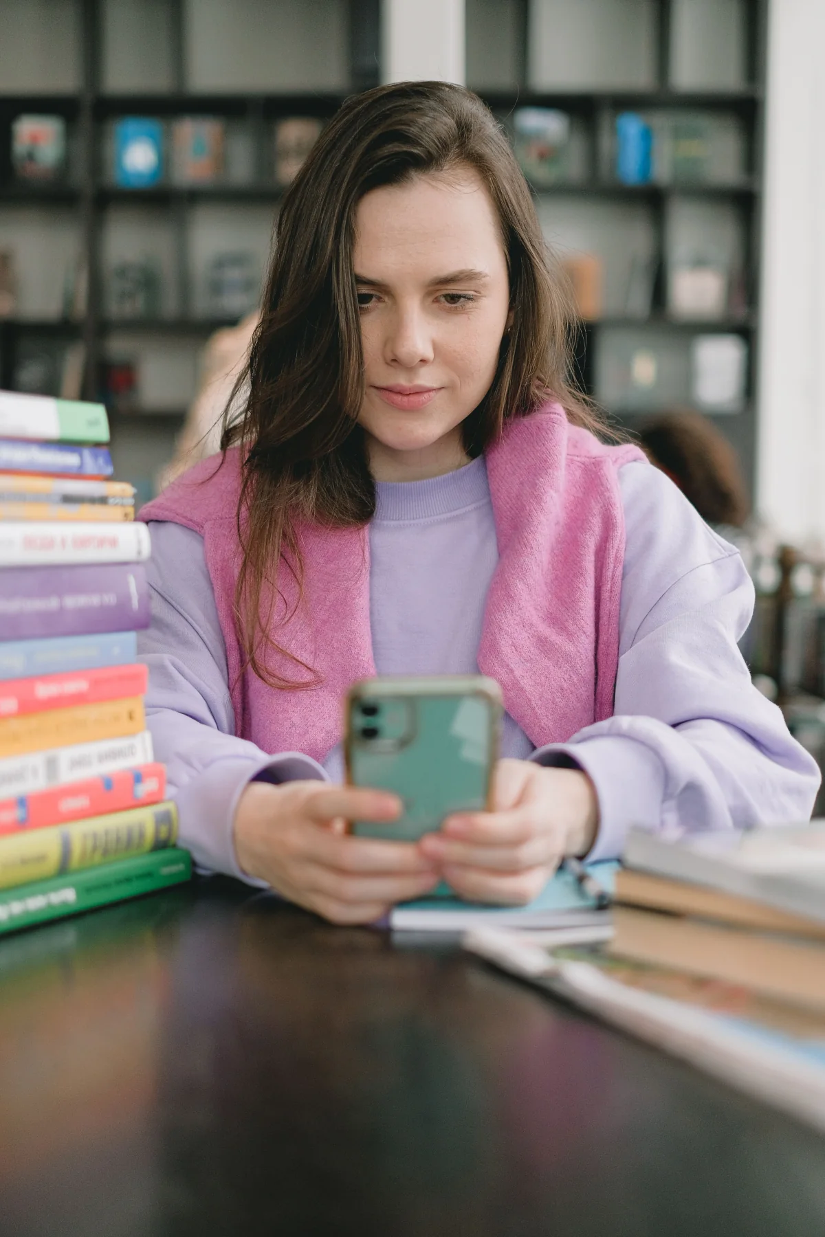 A high school student using a phone while studying in a library